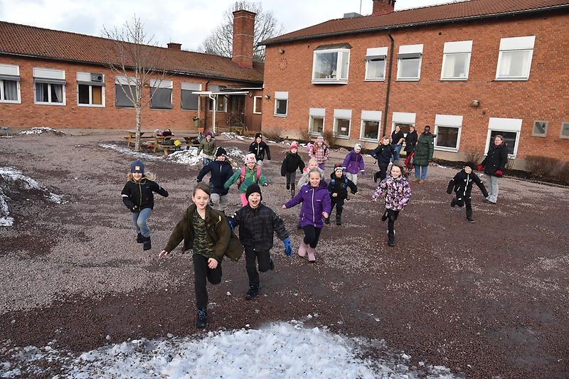 Barn springer framför skola