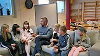 En man sitter tillsammans med sex barn i en soffa